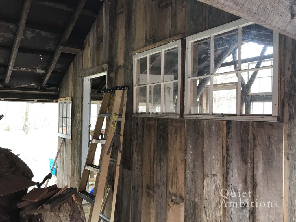 View of the old wood plank wall, with old windows, a stepladder and interior door. 