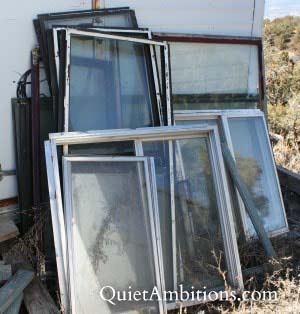 A pile of old windows stacked against a building.