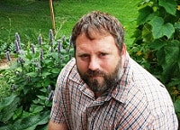 Brad sitting in his vegetable garden with plants visible behind him.